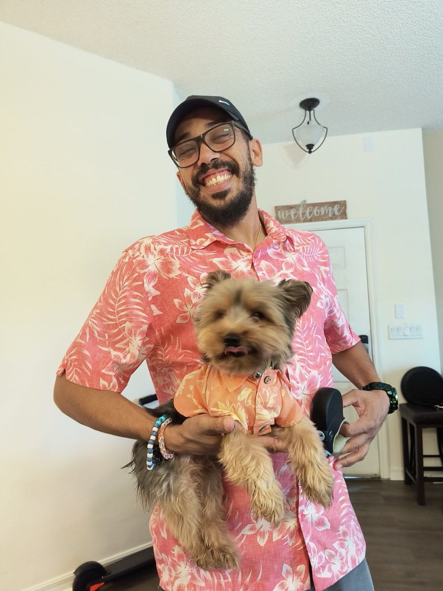 Erik Neal, founder of EZ Animal Care, smiling in a pink Hawaiian shirt and holding Prince Naveen the Yorkie