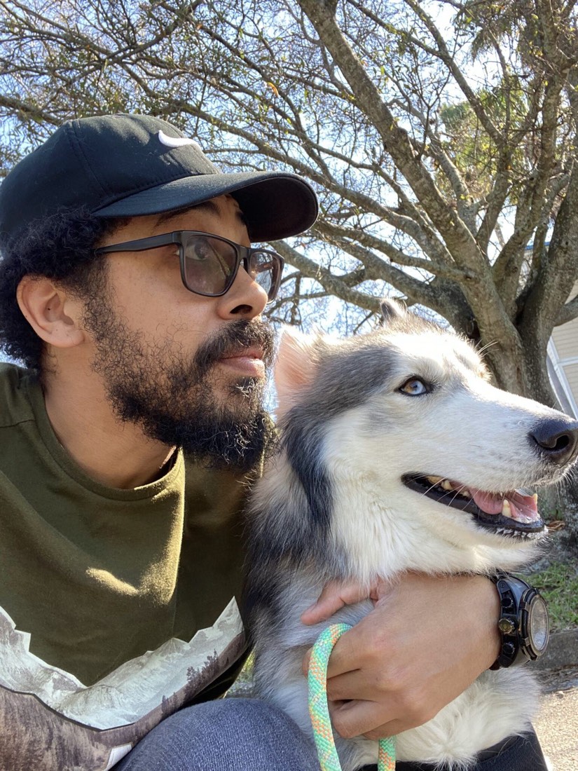 Erik outdoors in profile with his rescue Husky beside him under a tree in Broward County, Florida